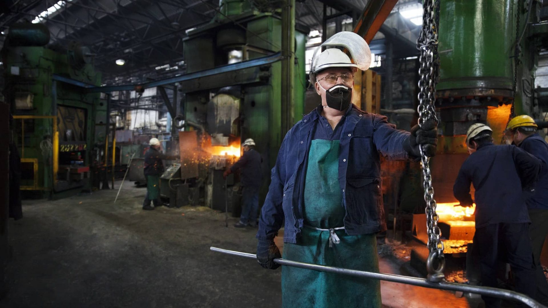 Operative prepares to hook steel billet out of furnace. Team in background using counterblow hammer